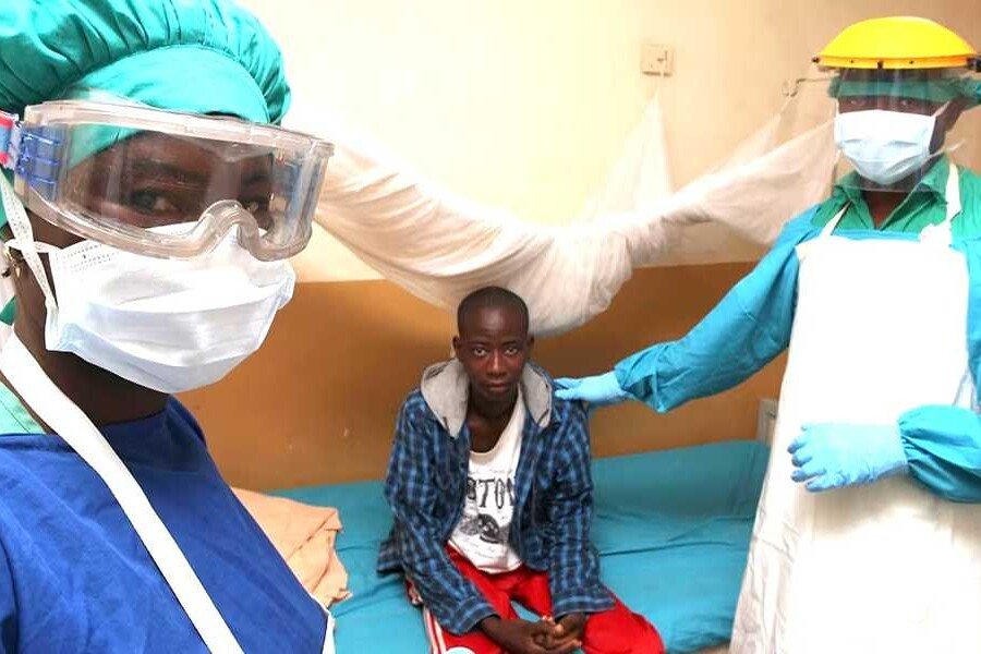 A picture of two health professionals dressed using universal precautions and a lassa fever patient